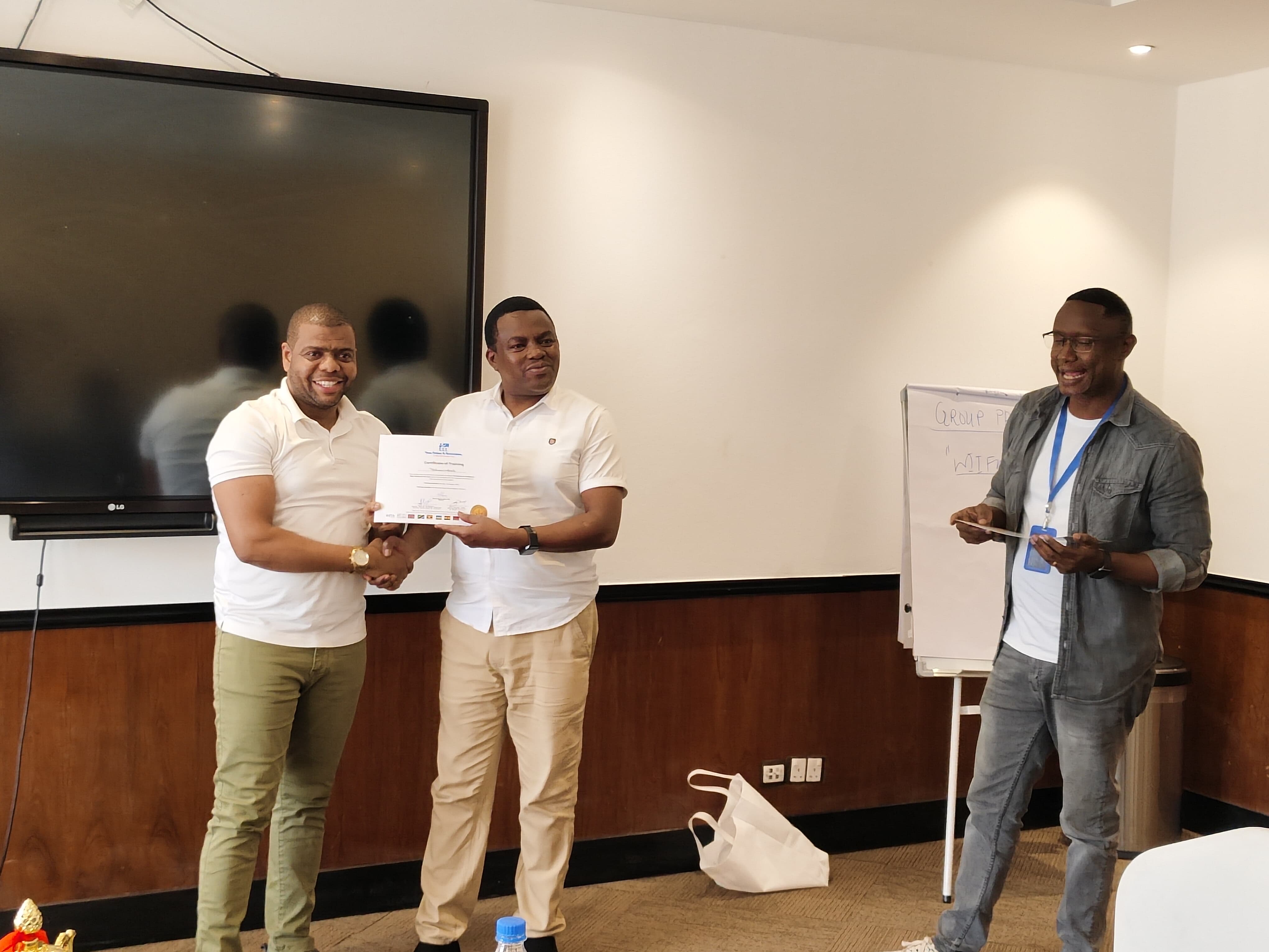 Participants shaking hands over a Certificate of Training while their facilitator looks on