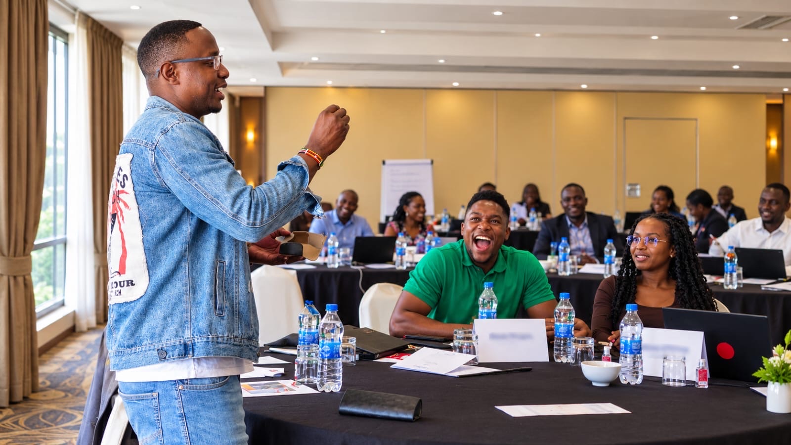 A facilitator leading an energetic training session as participants laugh and engage around conference tables