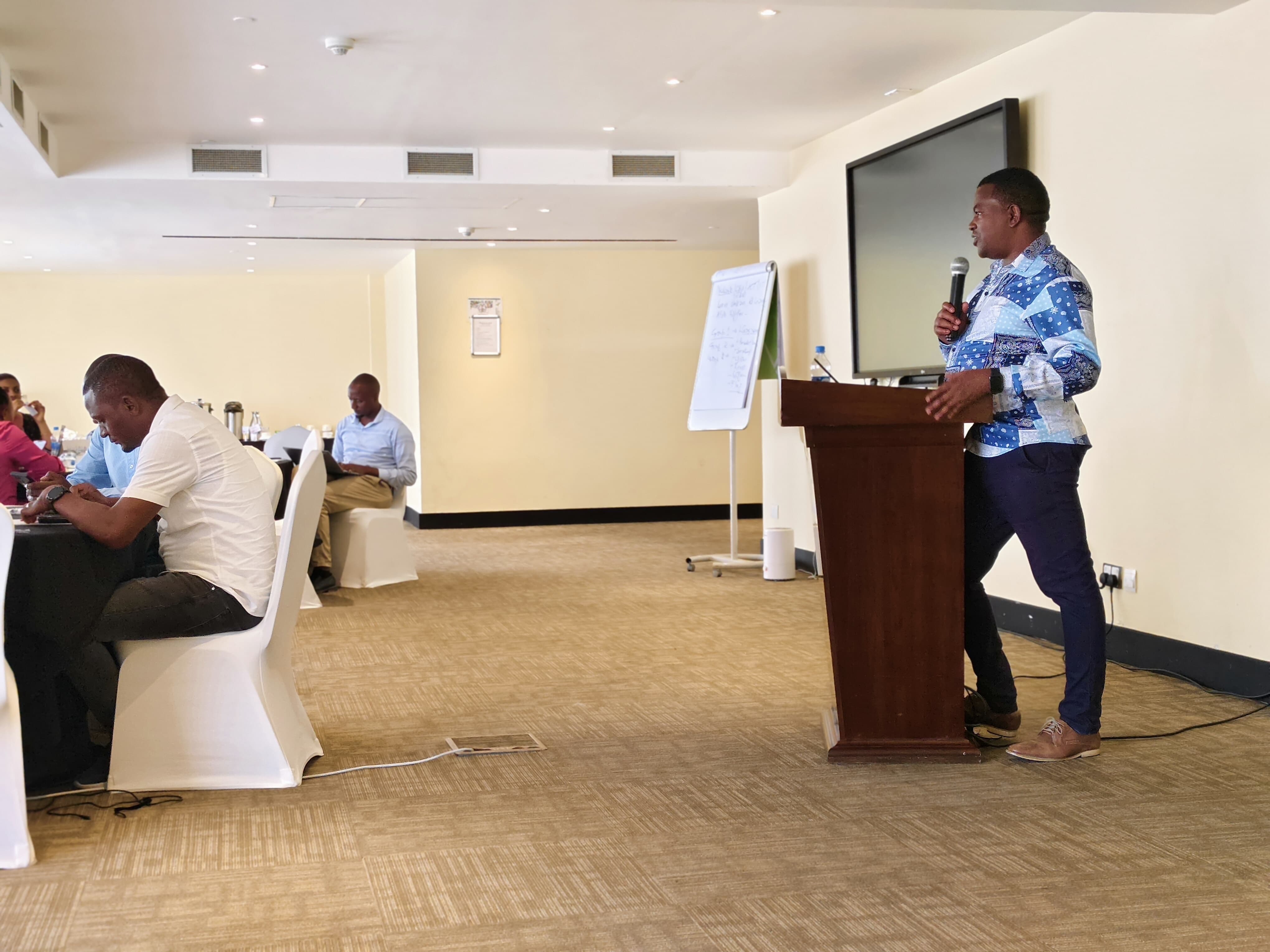 Facilitator speaking from a wooden podium to participants seated at round tables